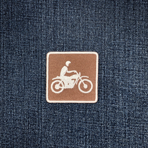Denim fabric with a brown patch featuring a white motorcycle and rider design.