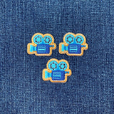 Three movie camera-shaped patches on a denim background