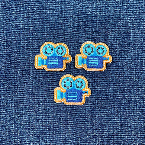 Three movie camera-shaped patches on a denim background