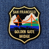 Shield-shaped patch depicting the Golden Gate Bridge in orange against a black sky, blue water, and green hills. Text reads: "SAN FRANCISCO GOLDEN GATE BRIDGE."