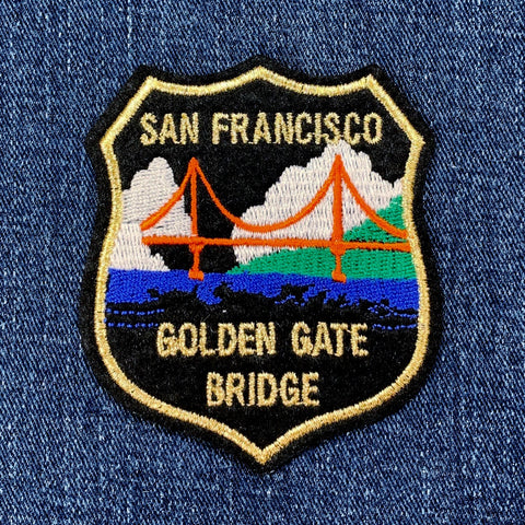 Shield-shaped patch depicting the Golden Gate Bridge in orange against a black sky, blue water, and green hills. Text reads: "SAN FRANCISCO GOLDEN GATE BRIDGE."