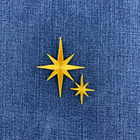 Two yellow star-shaped patches, one larger and one smaller, displayed on a blue denim fabric background.