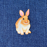 Embroidered patch of a brown and white bunny rabbit with pink ears on a denim background