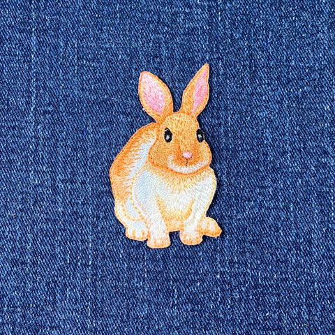 Embroidered patch of a brown and white bunny rabbit with pink ears on a denim background