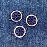 Three embroidered ship's wheel patches on a denim fabric background