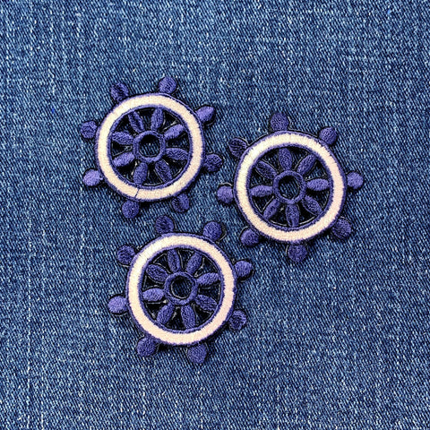 Three embroidered ship's wheel patches on a denim fabric background