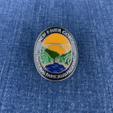 A medallion with an illustration of a bridge over a river, surrounded by mountain ranges, with text that reads 'NEW RIVER GORGE NATIONAL PARK AND PRESERVE' on a denim background
