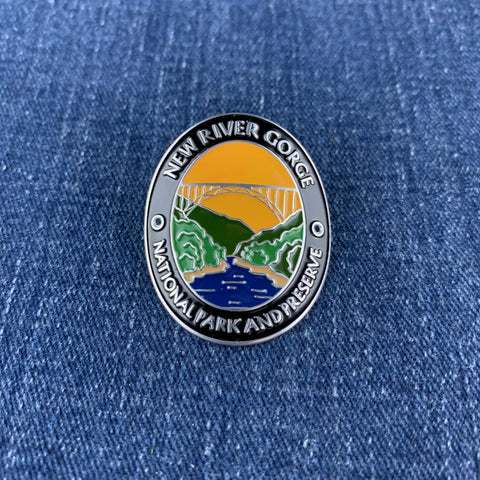 A medallion with an illustration of a bridge over a river, surrounded by mountain ranges, with text that reads 'NEW RIVER GORGE NATIONAL PARK AND PRESERVE' on a denim background