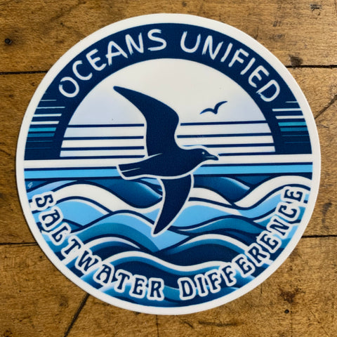 Sticker with 'Oceans Unified' design featuring a bird and ocean waves on a wooden background