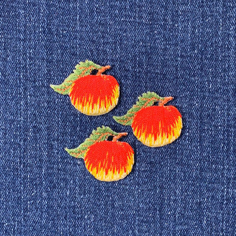 Three embroidered peach patches on a denim background