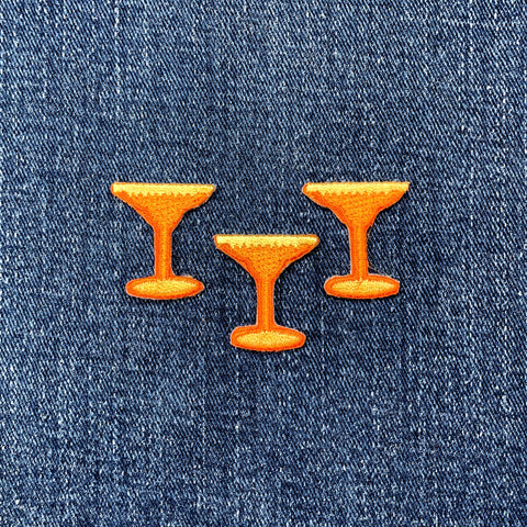 Three orange cocktail glass-shaped patches on blue denim fabric