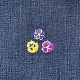 Three embroidered pansy flower patches on a denim background
