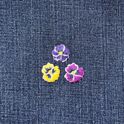Three embroidered pansy flower patches on a denim background