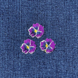 Three purple floral patches on a denim background