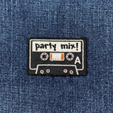 Embroidered patch of a cassette tape labeled 'party mix!' on denim fabric.