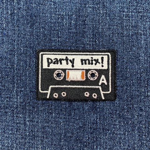 Embroidered patch of a cassette tape labeled 'party mix!' on denim fabric.