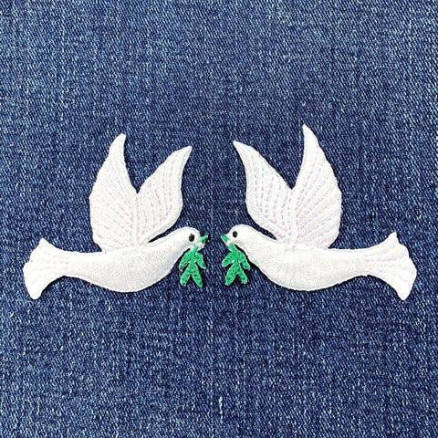 Two white dove patches with green leaves on a denim background