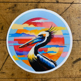 round sticker featuring a pelican with a colorful sky background on a wood table