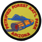 A circular embroidered patch for Petrified Forest National Park, Arizona, featuring a yellow background, red text, and a blue and orange log illustration with a black border.