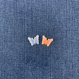 Two small butterfly-shaped patches placed on a textured blue denim background. 