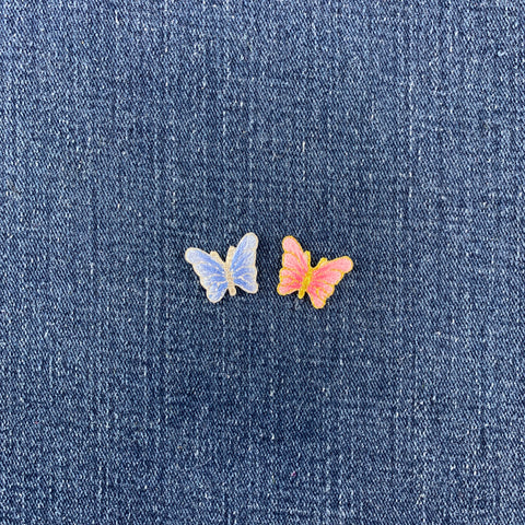Two small butterfly-shaped patches placed on a textured blue denim background. 