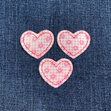 Three pink heart-shaped patches with floral patterns on a denim background