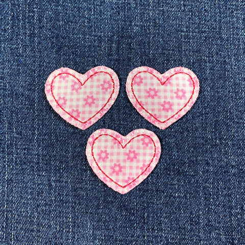 Three pink heart-shaped patches with floral patterns on a denim background