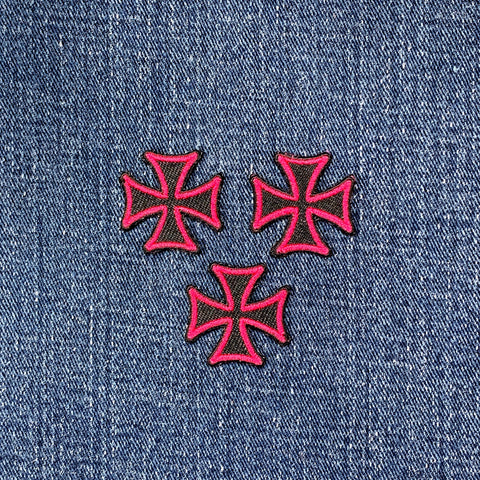 Three pink and black maltese cross patches on denim fabric
