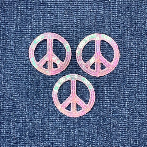 Three pink sequin peace sign patches on a denim background