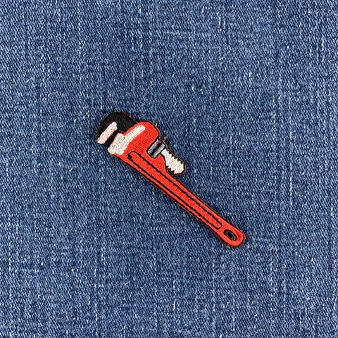 Red pipe wrench patch on denim fabric, designed for use with a plumber's uniform