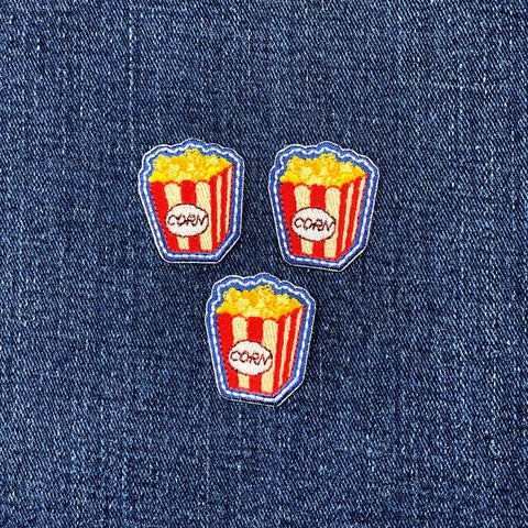 Three popcorn-themed patches on a denim background