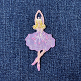 A shimmery embroidered badge of a ballet dancer in a purple tutu with pink accents and beads on a denim background