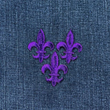 3 Purple embroidered fleur-de-lis patches on denim fabric