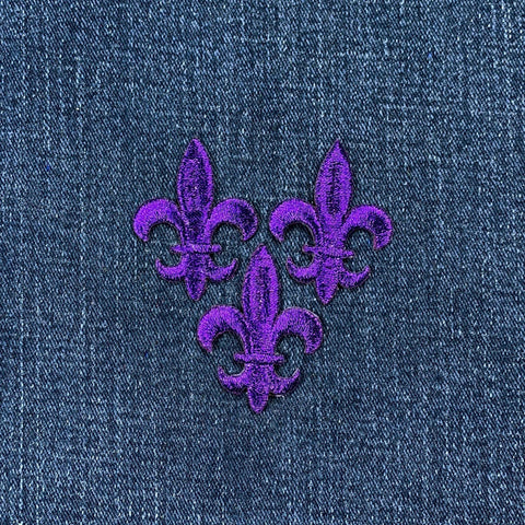 3 Purple embroidered fleur-de-lis patches on denim fabric