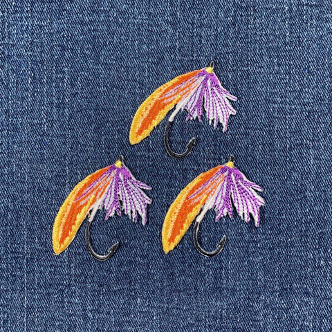 Embroidered fishing lure patches with orange and purple details on denim fabric