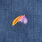 Fishing fly patch with orange, purple, and yellow colors on a denim background