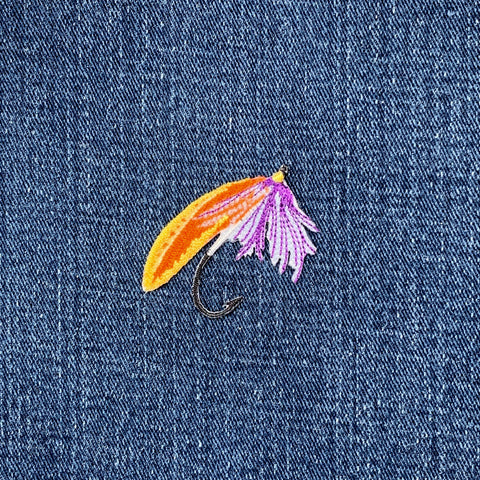 Fishing fly patch with orange, purple, and yellow colors on a denim background