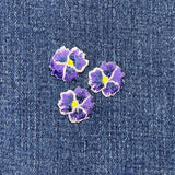 Three purple flower patches with yellow centers on a denim background