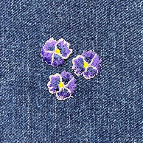 Three purple flower patches with yellow centers on a denim background