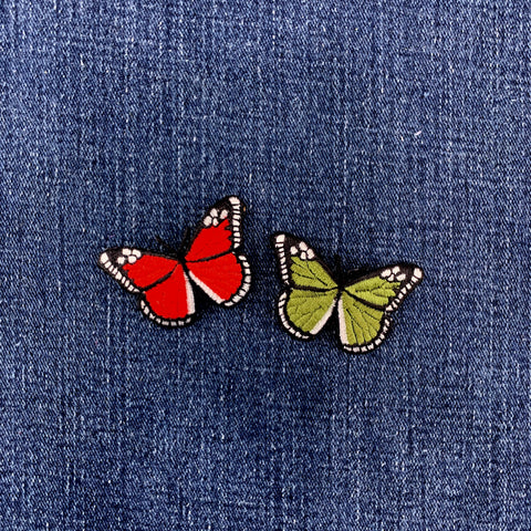 Two butterfly patches, one red and one green, on a denim fabric background.