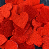 A pile of red embroidered heart-shaped patches with a textured, stitched appearance, filling the frame against a dark background.