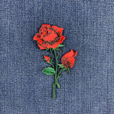 A patch depicting a red rose with buds and green leaves on a stem on a denim background