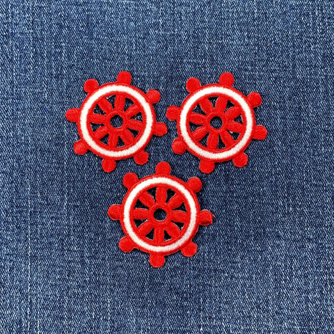 Three identical embroidered patches of a ship's wheel, colored bright red with a white outline around the rim, arranged on a denim background