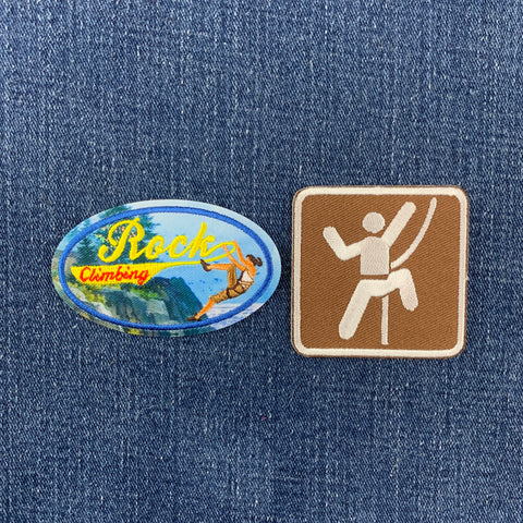 Two climbing-themed patches displayed on a blue denim background. The left patch is an oval blue and yellow design with the words 'Rock Climbing' and an illustration of a climber.