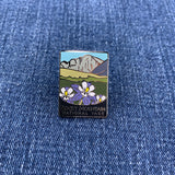 A pin badge featuring an illustration of mountains and flowers with the text 'Rocky Mountain National Park' on a denim background