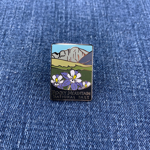 A pin badge featuring an illustration of mountains and flowers with the text 'Rocky Mountain National Park' on a denim background