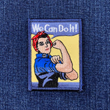 A patch featuring an embroidered depiction of Rosie the Riveter with the slogan 'We Can Do It!' in a vintage WW2 style.