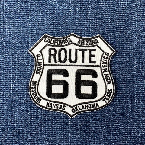 A shield-shaped patch with 'ROUTE 66' written in bold letters, surrounded by the names of US states in a circular pattern, and a badge number '66' in the center.