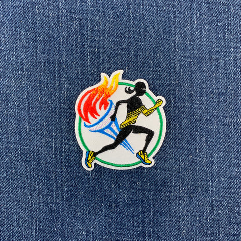 A patch featuring a running track and field motif with a silhouette of a marathon runner, a torch, and a track and on a denim background