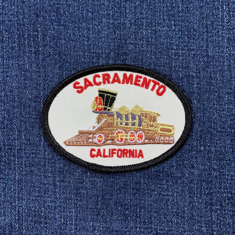 Oval embroidered patch featuring a brown and gold vintage steam locomotive. Red text reads "SACRAMENTO" above and "CALIFORNIA" below.